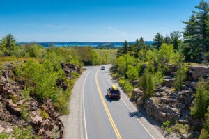 Cars driving on road in Acadia National Park, Maine, USA. One car holds a canoe on its roof. Credit: iStock