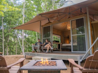 Two people sitting on a glamping tent porch in Maine at Point Sebago Resort.
