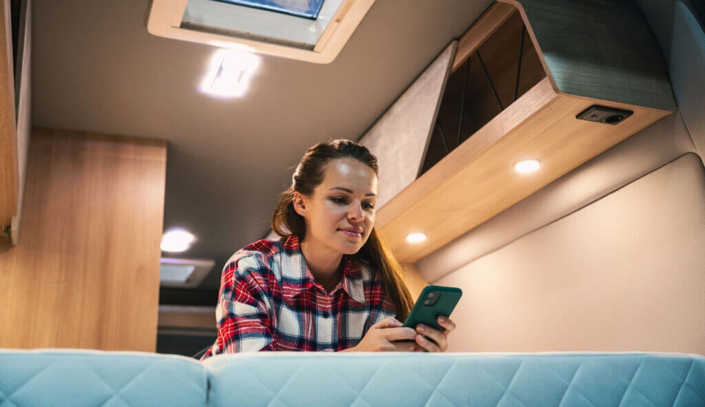 Woman relaxing on bed inside motorhome and checking her smart phone | Credit - iStock