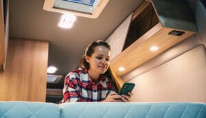 Woman relaxing on bed inside motorhome and checking her smart phone | Credit - iStock