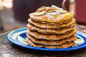 Stack of pancakes on a blue plate topped with bananas and nuts