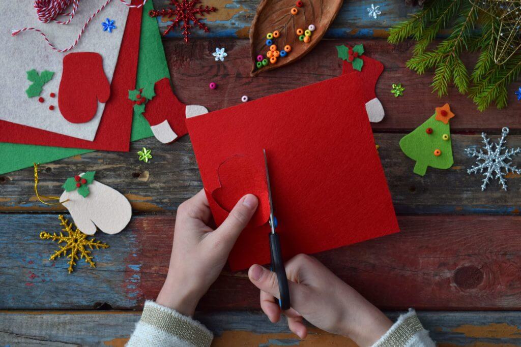 Hands using scissors to cut red felt on a wooden table