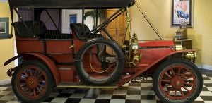 Red antique car displayed in museum on a black and white checkered floor