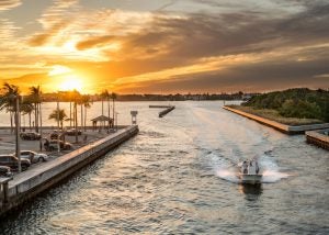 Boat driving down the water with sunset and palm trees behind it