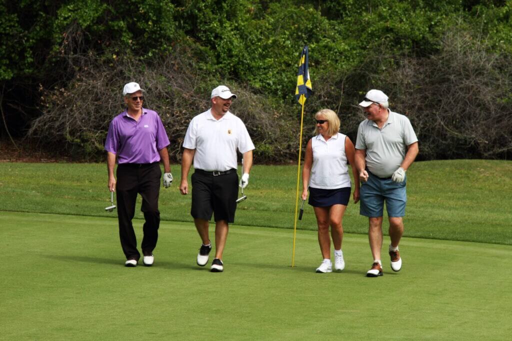 four golfers walking on green away form the hole talking