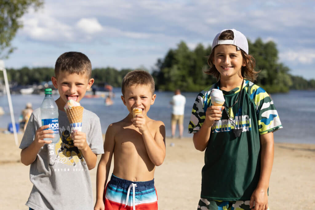 Three boys eating ice cream on the Sebago Lake beach at Point Sebago Resort in Maine.