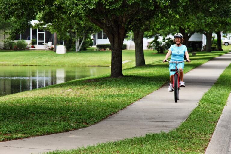 Woman riding a bike on the sidewalk next to lake at Bear Creek Village.