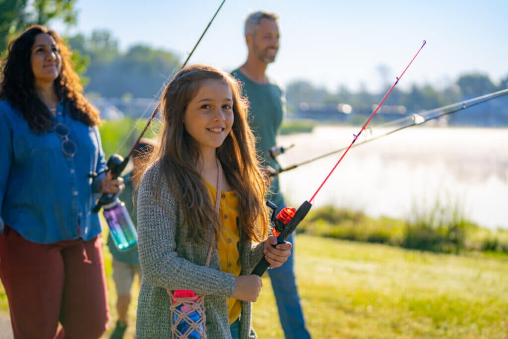 CKF Family Fishing 55 Girl holding a fishing pole with her parents behind her at CreekFire RV Resort in Savannah, Georgia.