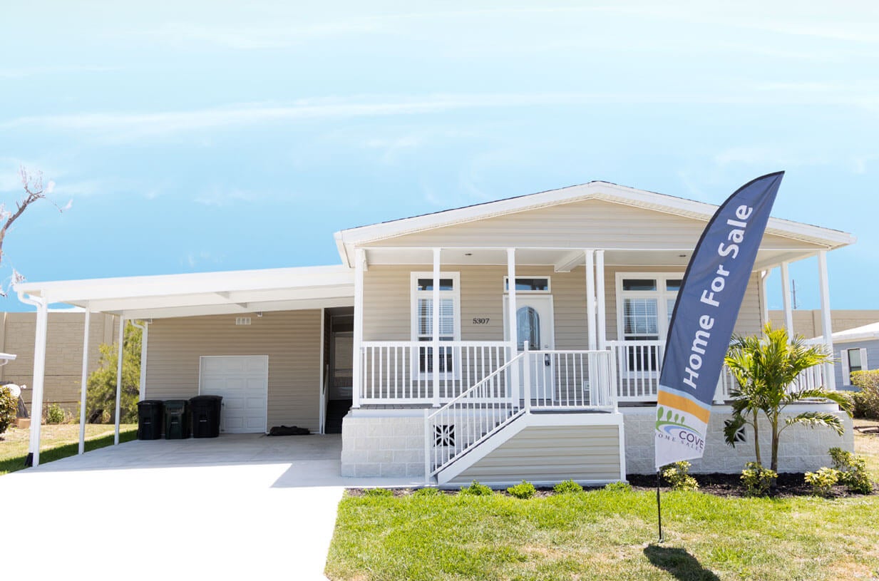Manufactured home with "home for sale" flag waving in the front yard at Camelot Lakes Village in Sarasota, Florida