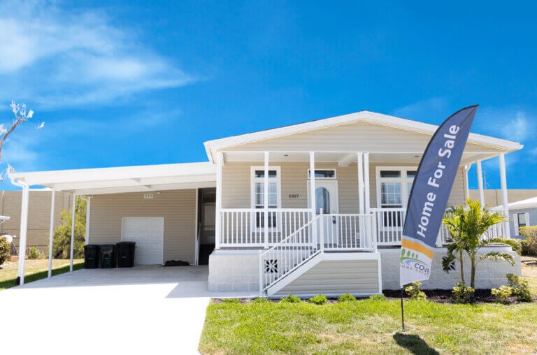 Manufactured home with "home for sale" flag waving in the front yard at Camelot Lakes Village in Sarasota, Florida