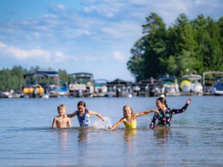 Four kids swimming in Sebago Lake at Point Sebago Resort in Maine with the marina and boats in the background.