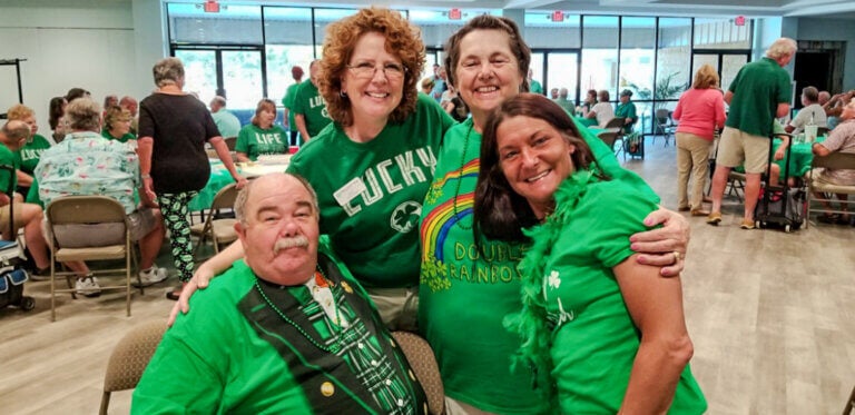 Four residents in green shirts, two men and two women, pose for a photo at a St. Patrick's Day event in Rolling Greens village 55+ community.