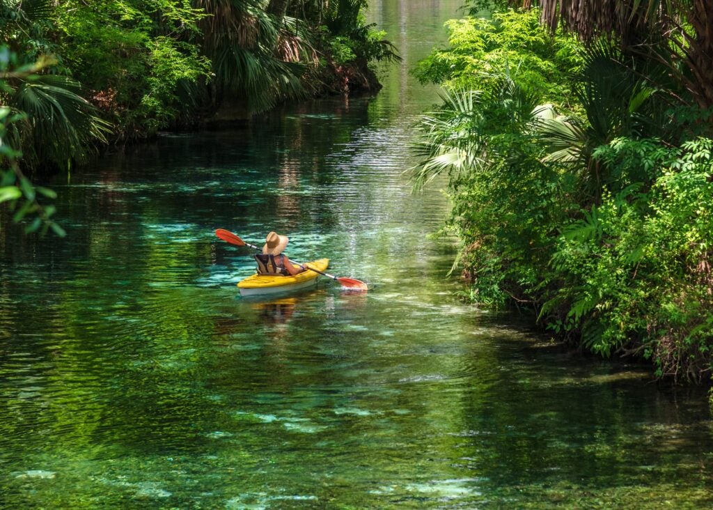 woman in sun hat paddling in a yellow kayak