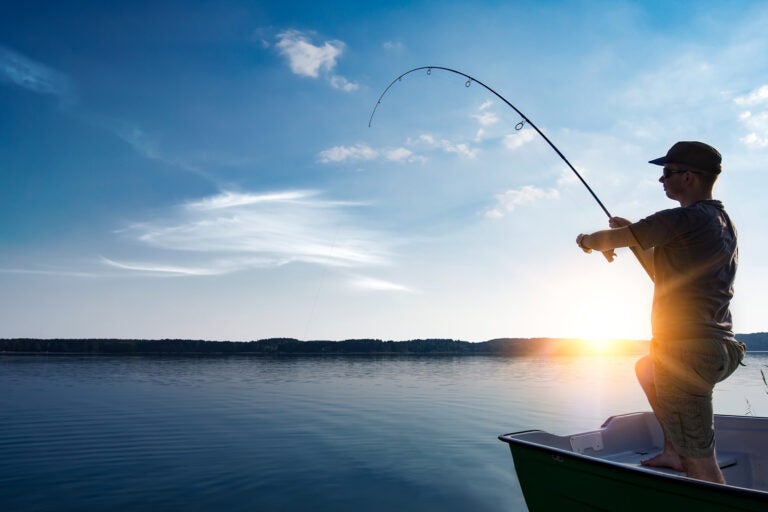 man fishing on lake with sun on horizon