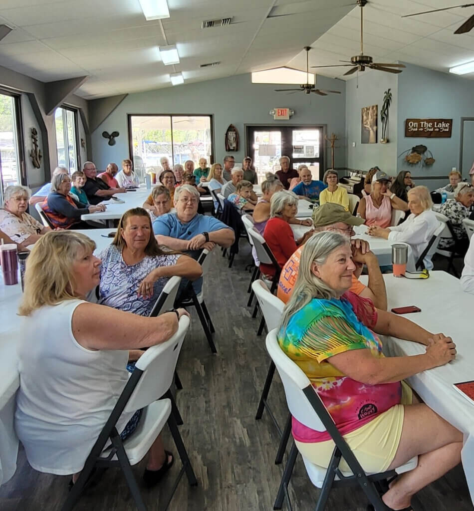 A large group of Holiday RV Park Ambassadors are seated in the Marina for a meeting.