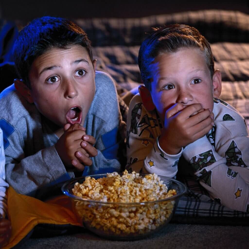 two boys eating popcorn watching a scary movie