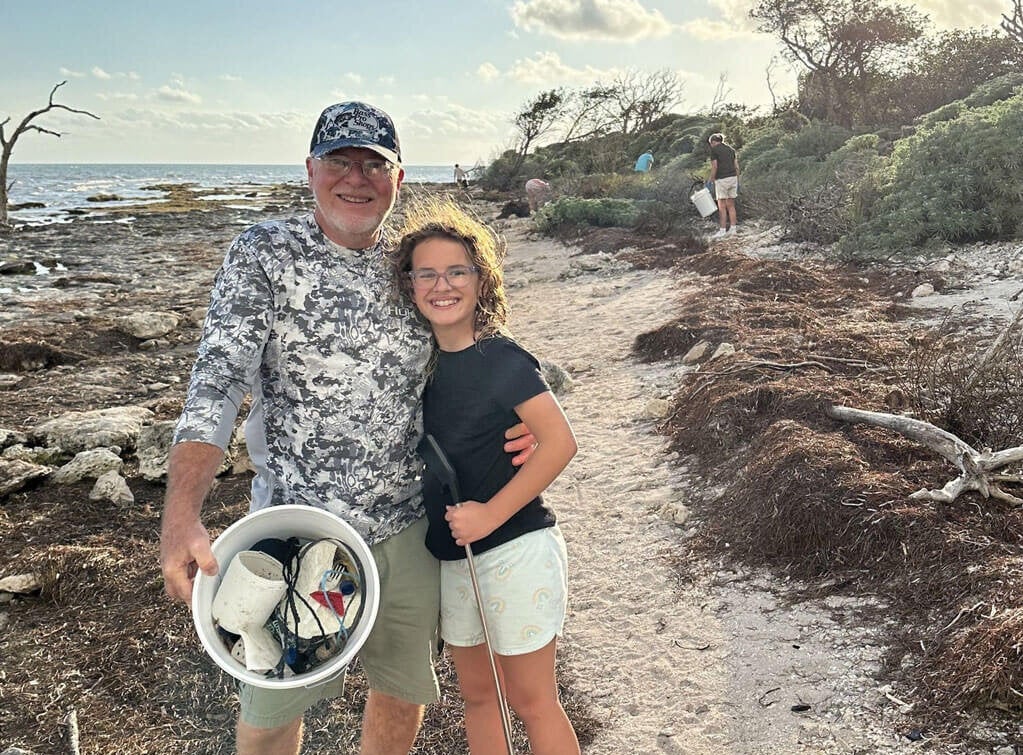 Man and a little girl picking up trash along the shoreline at Big Pine Key in Florida.