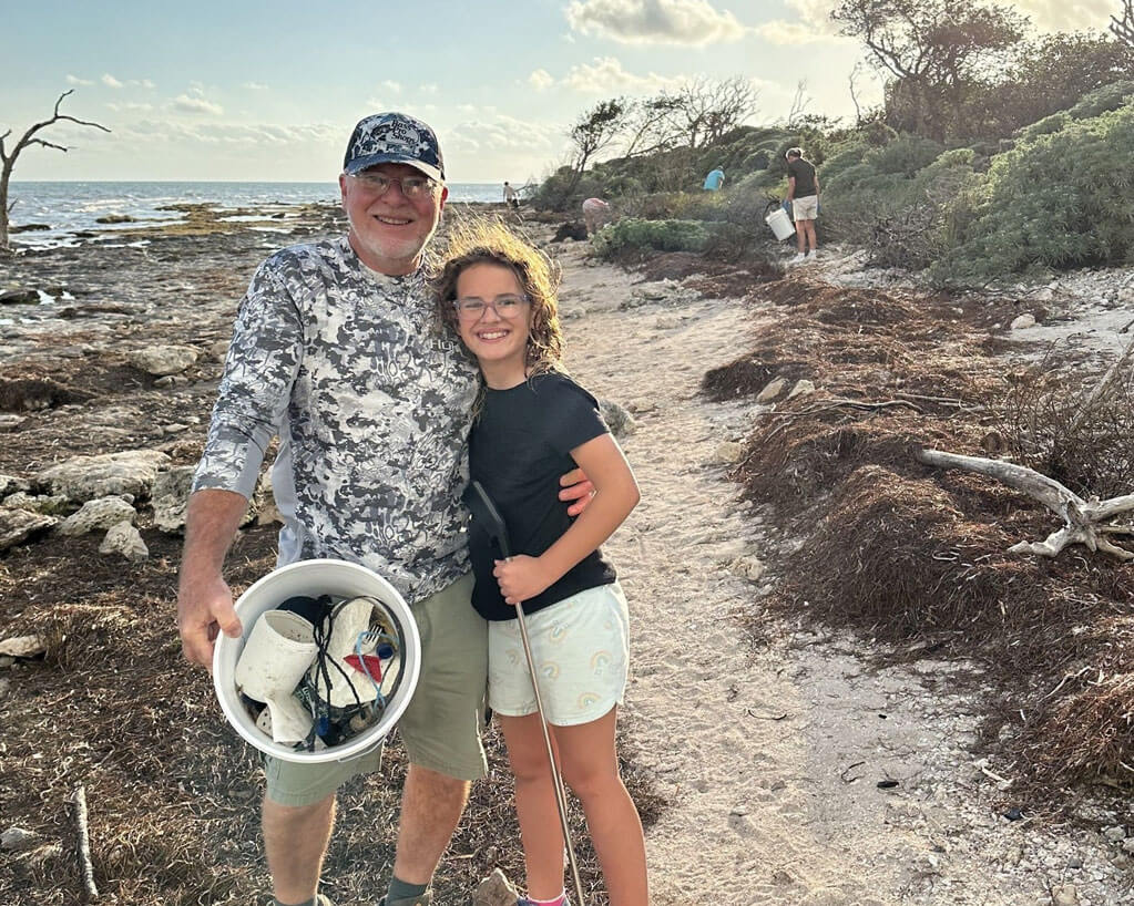 Man and a little girl picking up trash along the shoreline at Big Pine Key in Florida.