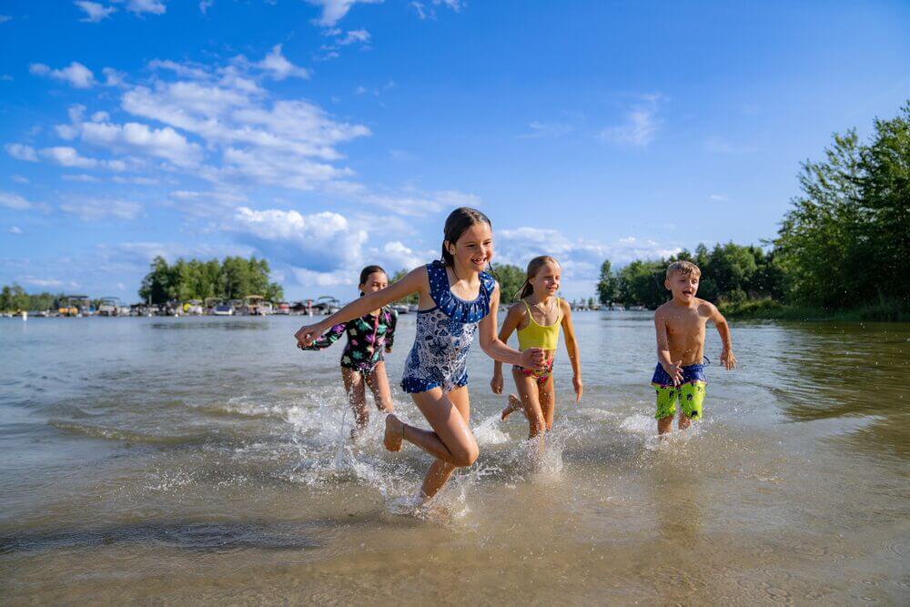 Kids running from Sebago Lake onto the beach at Point Sebago Resort in Maine.