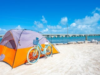 Big Pine Key- Rustic Tent An orange tent sitting next to a turquoise bicycle on the beach overlooking the water at Bg Pine RV Park in Florida.