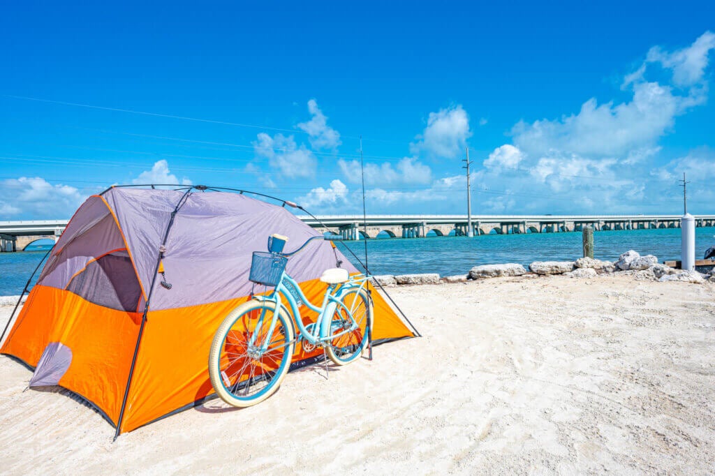 An orange tent sitting next to a turquoise bicycle on the beach overlooking the water at Bg Pine RV Park in Florida.
