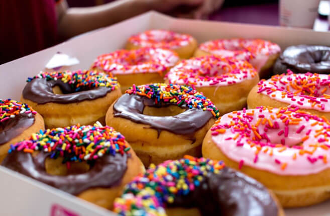 Box of glazed donuts with colorful icing and sprinkles.