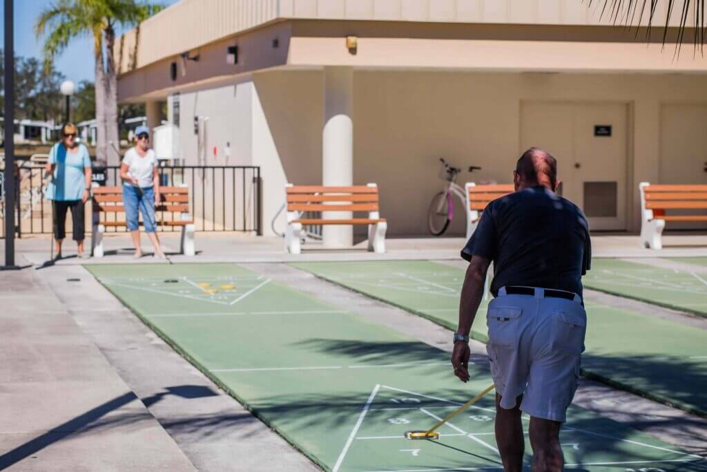 Three people playing shuffleboard at Camelot East Village in Florida.