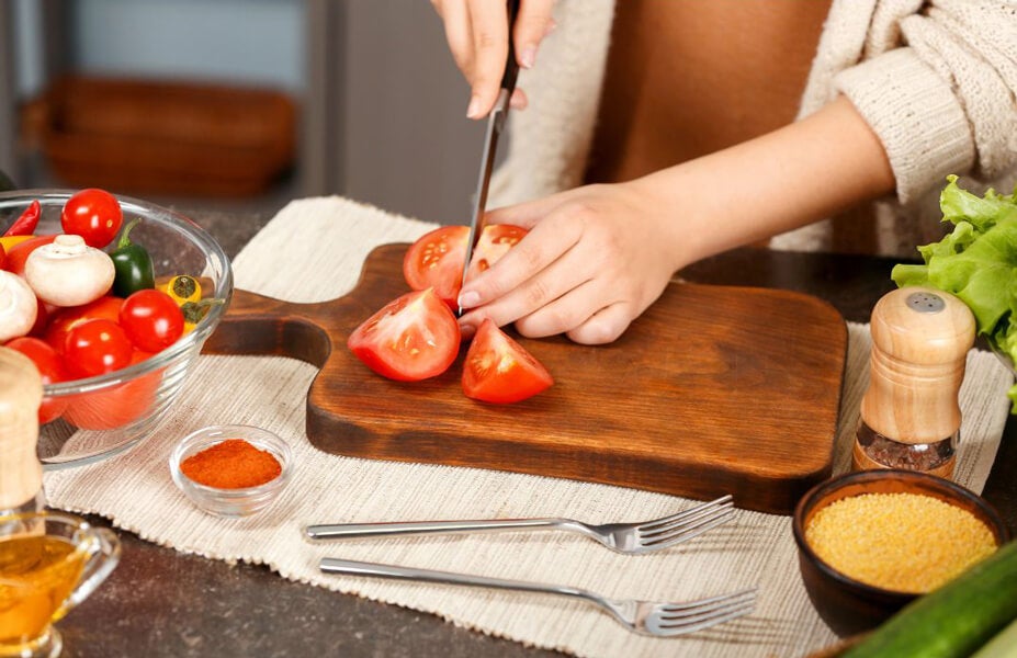 Hands Cutting Tomatoes at Table in Kitchen