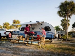 Two people outside small camper at picnic table.