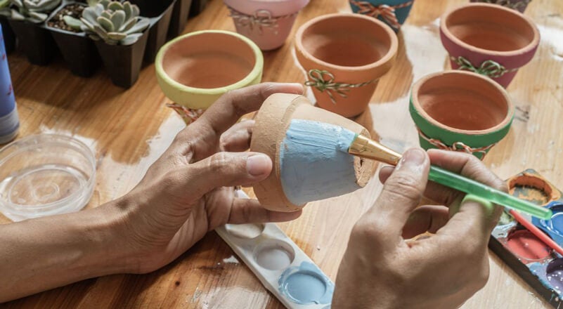 Person painting a terracotta flower pot a baby blue color