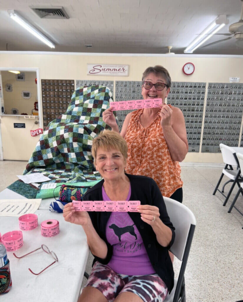 Two members of the Quilt Club holding raffle tickets at a club event