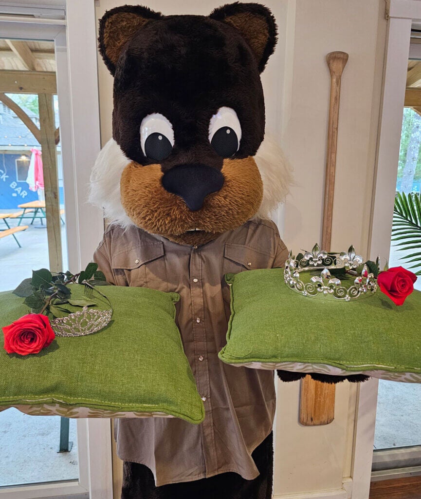 Chippy the Point Sebago mascot holding two homecoming crowns and roses on green pillows.