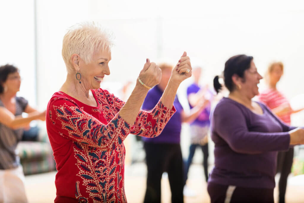 Beautiful senior woman snaps her fingers as she learns new dance moves during dance class at her senior center. People are dancing in the background. Credit: iStock