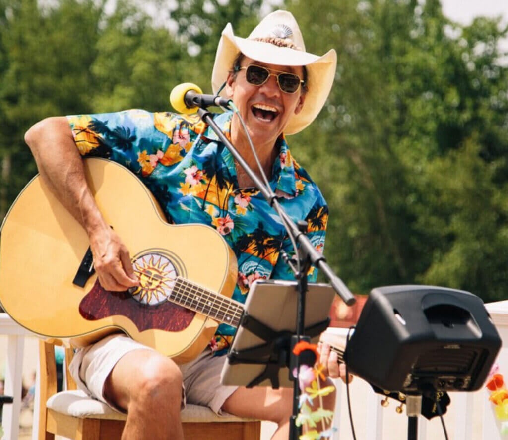 guy in Hawaiian shirt sitting in a chair strumming guitar and singing