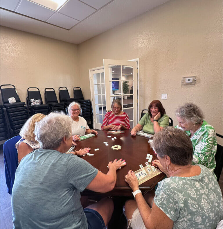 guests gathered around a table in the clubhouse playing dominoes