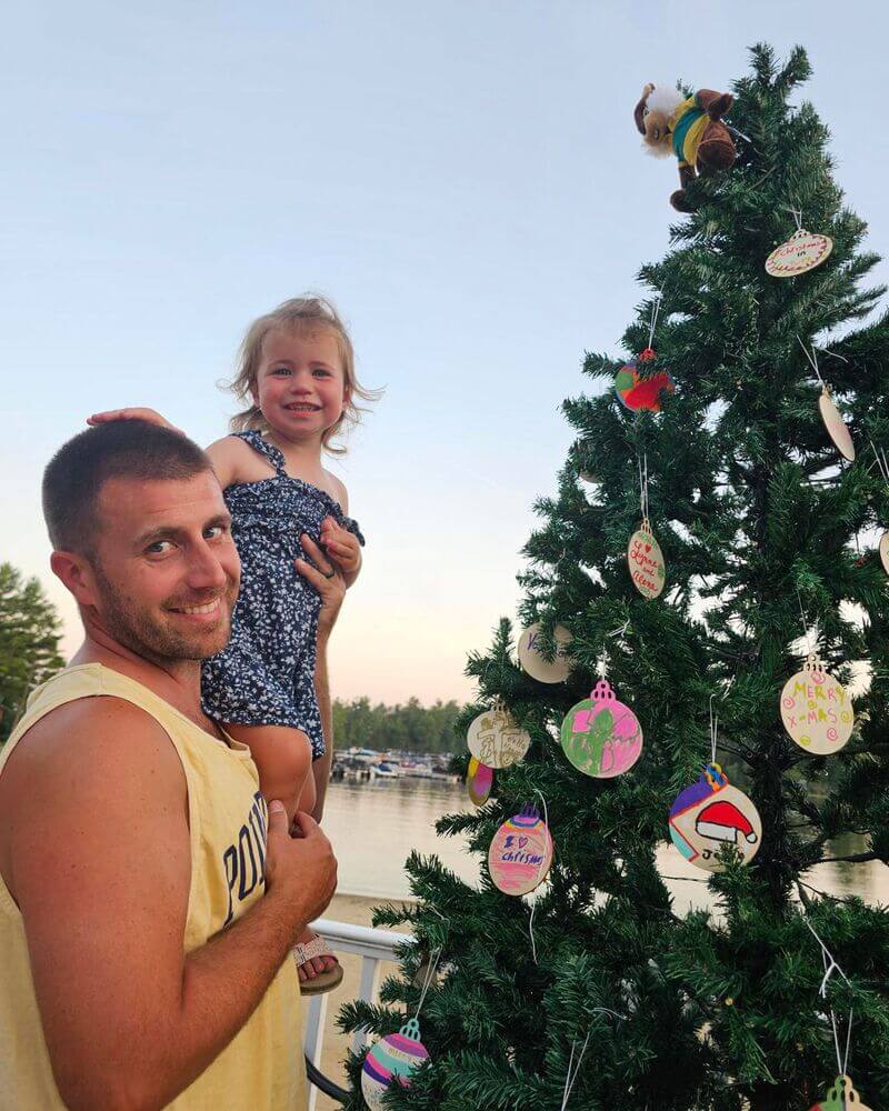 Christmas in July tree covered in ornaments with a man and a little girl next to it at Point Sebago Resort in Maine.