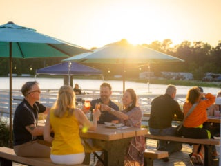Group of people eating at the picnic tables at sunset in front of CreekFire RV Resort's Lakehouse restaurant.