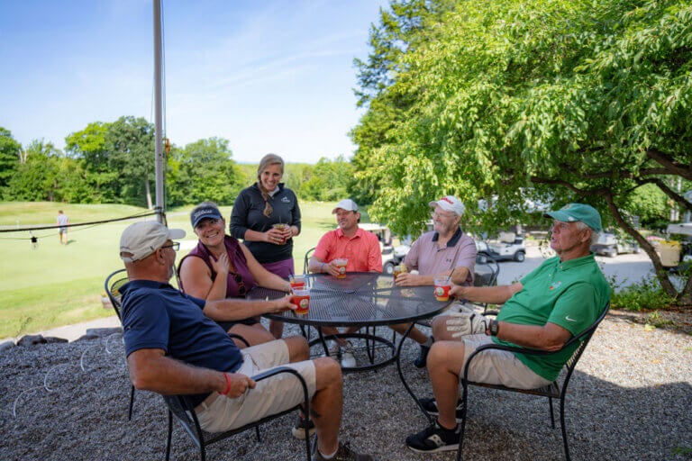 Golfers sitting around a table drinking beer outside at the 19th Hole in Casco, Maine. The restaurant is part of the Point Sebago Golf Course.