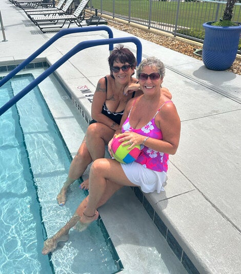 Two 55+ residents sitting on the steps in the swimming pool at Rolling Greens Village in Ocala, Florida.