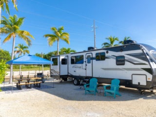 RV Big Pine Key A fifth wheel rental trailer parked next to the canal at Big Pine Key RV Park. There are two turquoise chairs outside the trailer.
