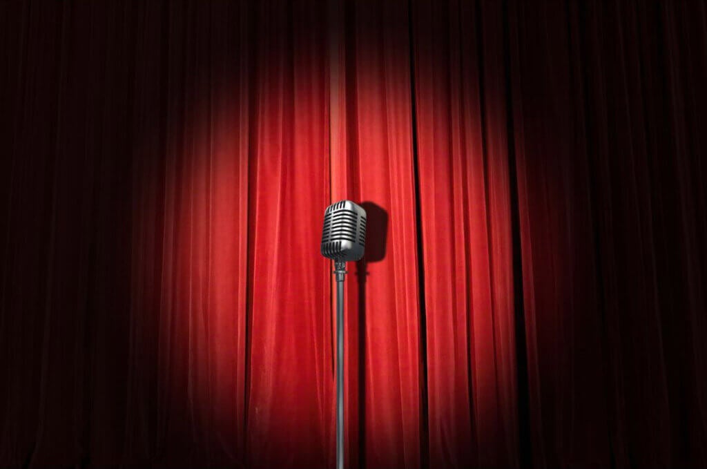 Red curtains closed on a stage with a spotlight on a microphone