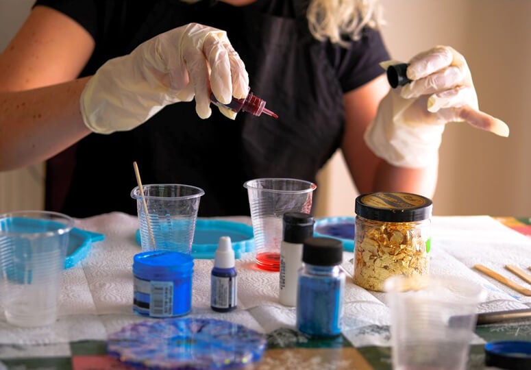 Close-up of a person wearing gloves, surrounded by art supplies working on a resin art project.