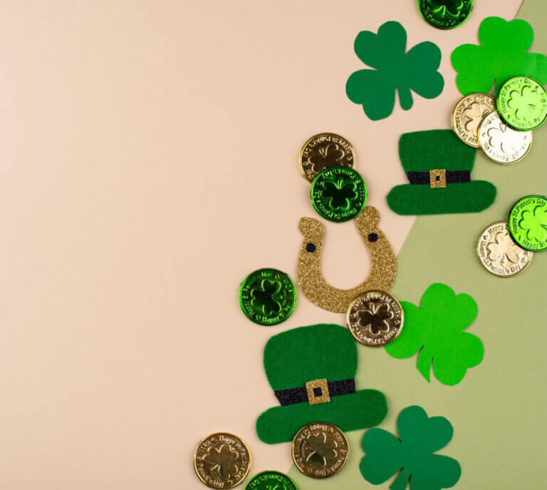 St. Patrick's Day decorations including green shamrocks, gold coins, green hats, and a gold horseshoe scattered on a two-toned background.
