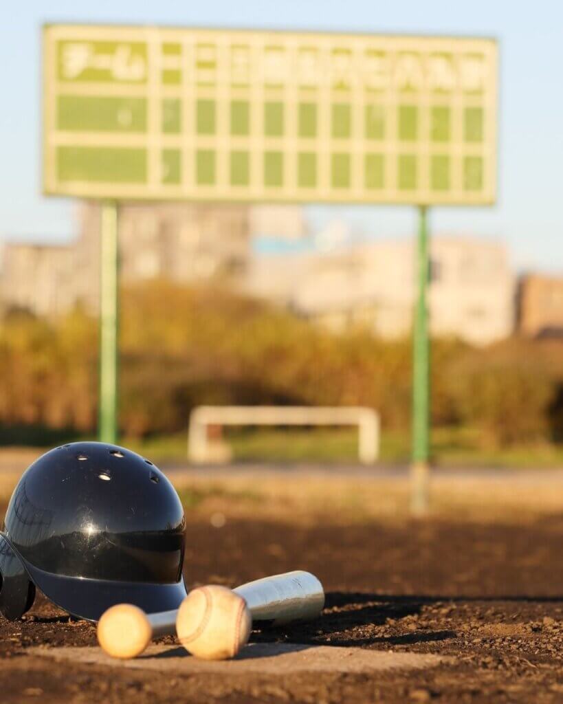 Stock photo of a baseball hemet, bat, and baseball laying on field.