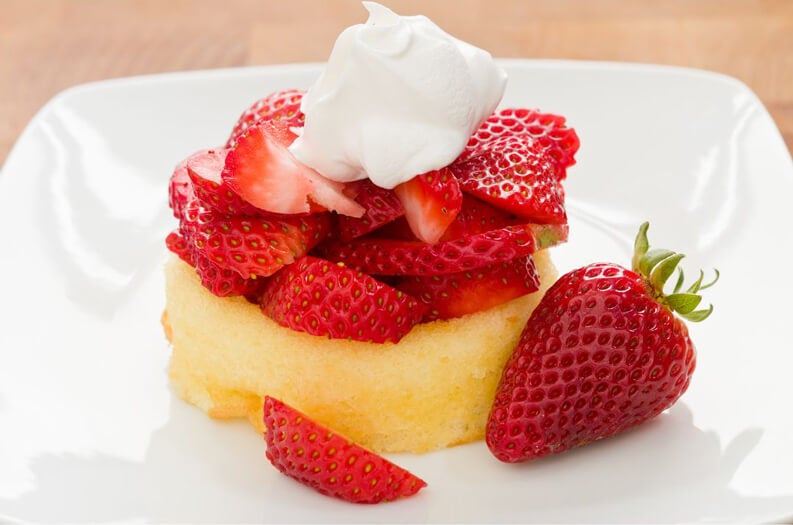 close-up of a shortcake topped with sliced strawberries and whipped cream.