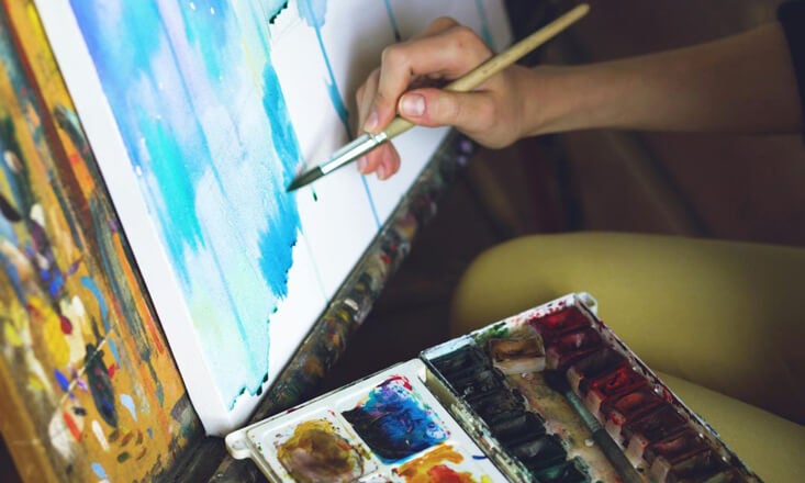 Person painting a canvas different shades of blue and green.