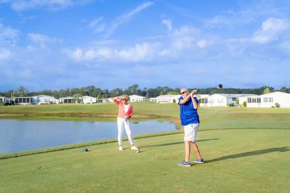 Couple playing golf at Big Cypress Golf Club with manufactured homes in the background.