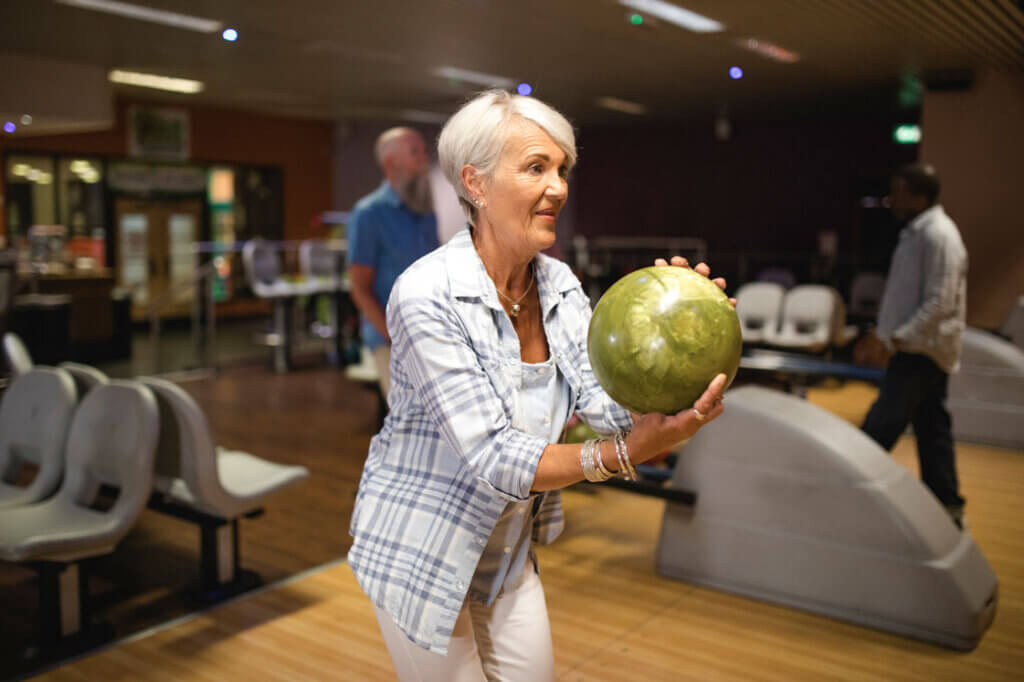A senior woman is taking her turn at ten-pin bowling.