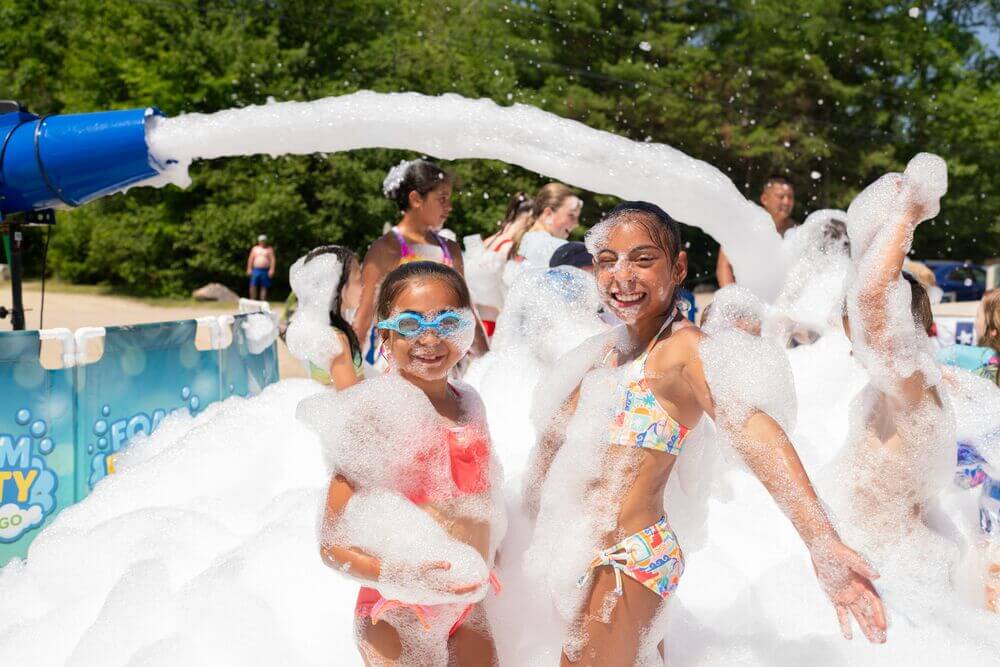 Two girls playing in foam on the beach at Point Sebago Resort in Maine.