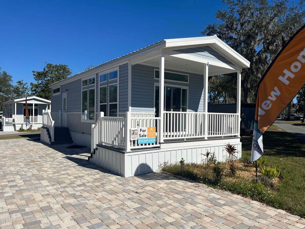 A manufactured park model home with a front porch and two for sales signs inside Holiday RV Park in Leesburg, Florida.